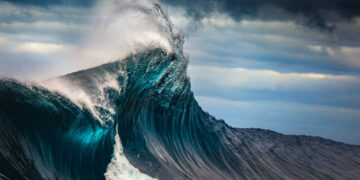 Tall powerful cross ocean wave breaking during a dark, stormy evening.